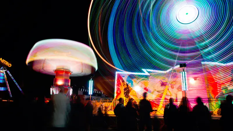 Spinning fairground rides lit up at night with a crowd in silhouette