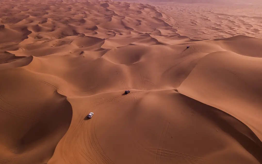 Aerial view of 4x4 vehicles crossing red desert dunes