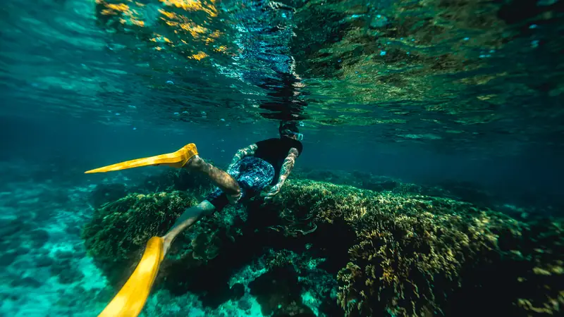 Snorkeller in fins swimming over a reef in clear turquoise water