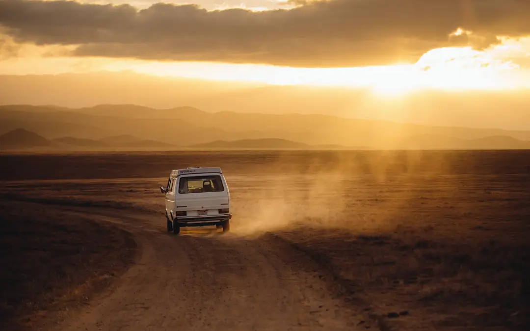 Vehicle driving across a dusty desert track at sunset