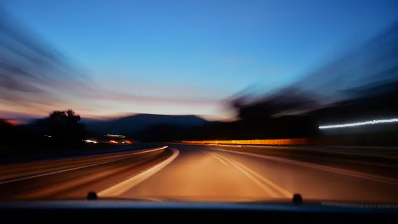 Road at dusk blurred by speed from inside a moving car