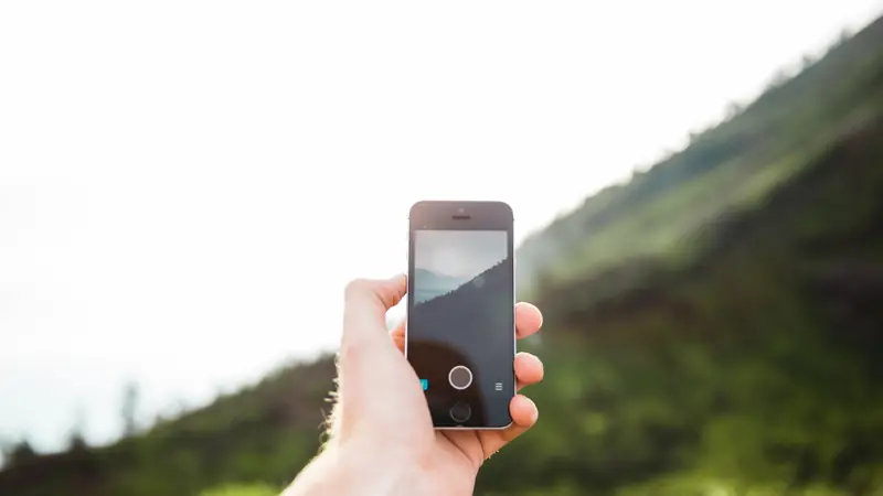 Hand holding a smartphone against a green hillside