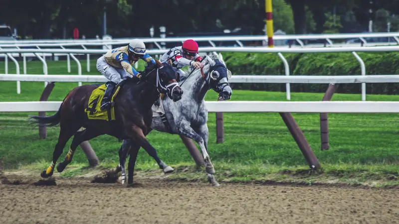 Two racehorses and jockeys galloping side by side on a dirt track
