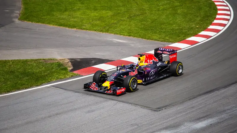 Open-wheel race car taking a corner beside red and white kerbs