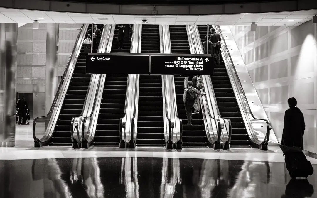 Row of airport escalators in black and white with travellers heading down