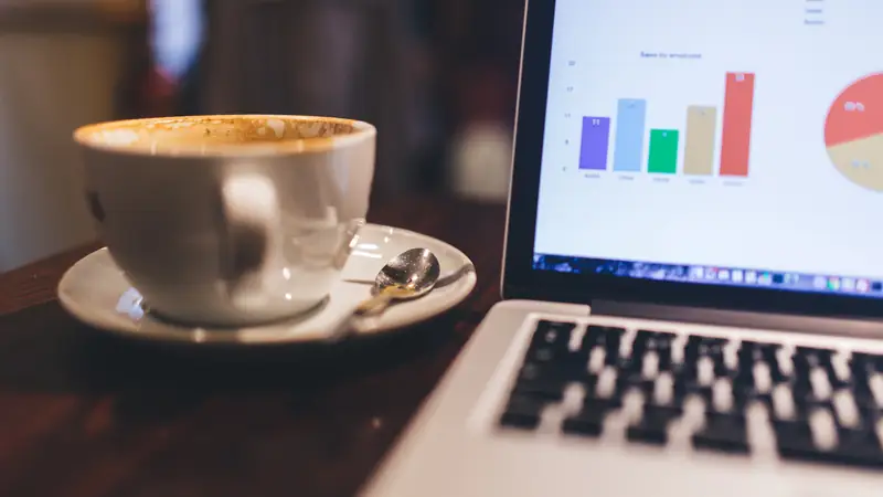 Cup of coffee beside an open laptop showing charts